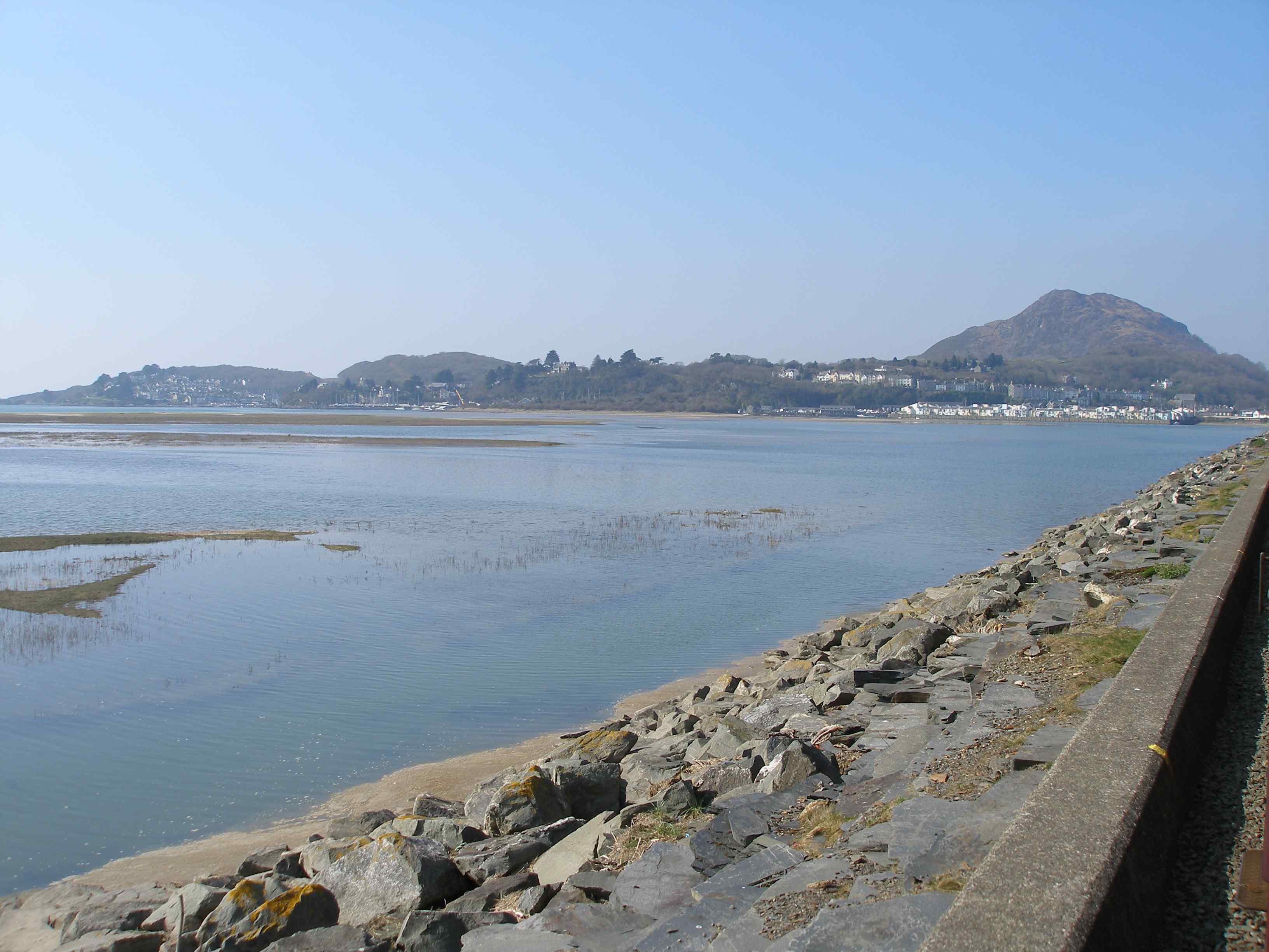 The view across the Cob from either side of the train is spectacular. In this case Borth-y-Guest and the marina at Porthmadog are in view looking northwards as the train heads back to Harbour Station. For those who have followed the Michael Portillio railway journey programmes, there's a quick glimpse from this same spot but looking out to sea that appears in the opening sequence. The wave wall built in 1940 in an attempt to reduce flooding can be seen to the left of the train.