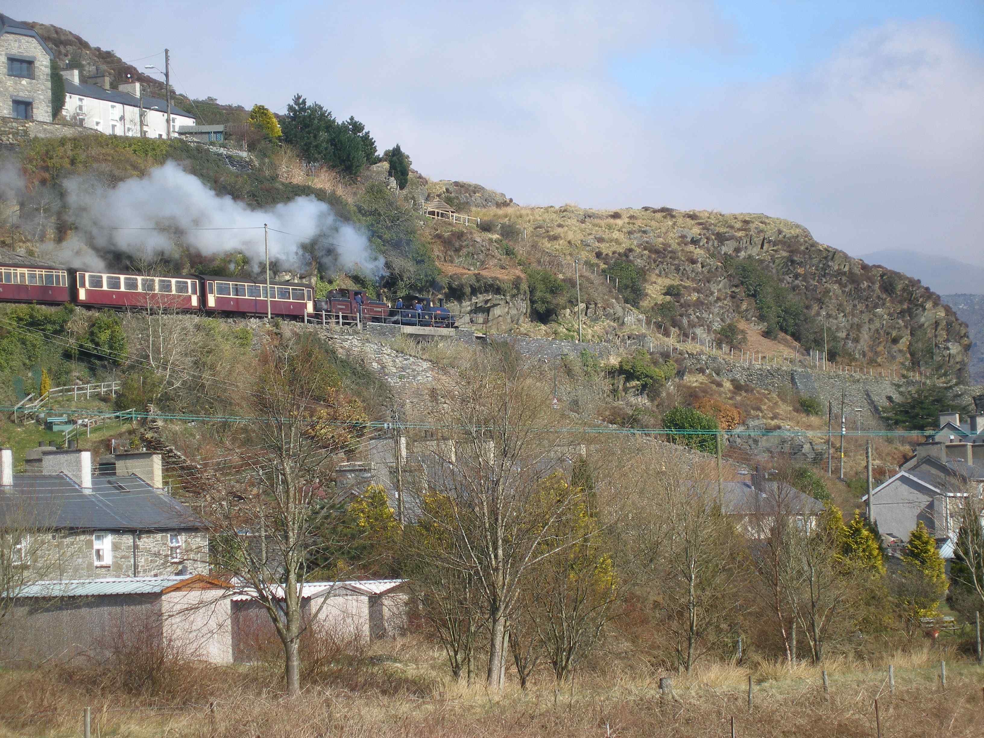 'Merddin Emrys' and 'Linda' make a splendid site working their way northwards over the village of Tan-y-Grisiau ('Under-the-steps' in Welsh). 'Linda' is in plain black, reflecting a loco only just out of the workshops. I remember walking down this section in 1970 and not really believing trains would ever be restored. The train is just crossing a road bridge which the council removed during closure and raised the road level - also believing that trains would not be restored! On restoration, road vehicle access was engineered from a totally new location away from the railway.