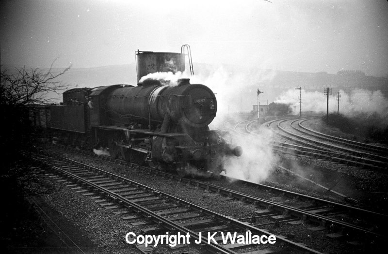 WD Austerity 90217 stands by the water tank at Stansfield Hall Junction with a loaded mineral train, whilst a banker can be seen in the background.