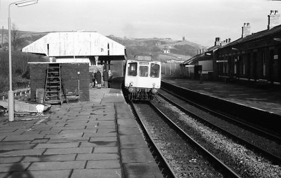 A three-car Class 110 heading for Leeds stands at the eastbound platform 2 at Todmorden railway station, after the canpoy has been removed from platform 1, but the easterly canpoy on platform 2 and the station master's house still stand The class 110 'Calder Valley'unit displays a '0000' headcode.